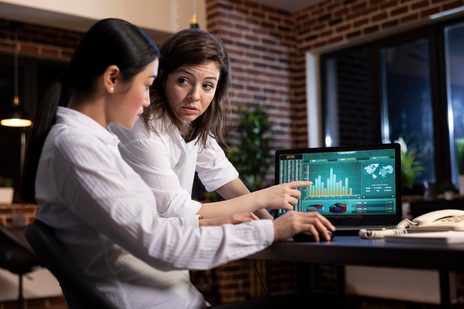 Two women analyzing financial data on a laptop